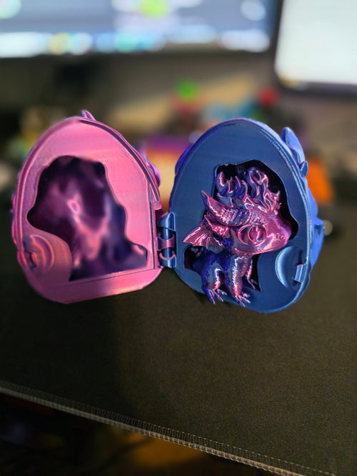 3D printed dragon egg locket open showing metallic pink baby dragon inside blue egg shell, angled view